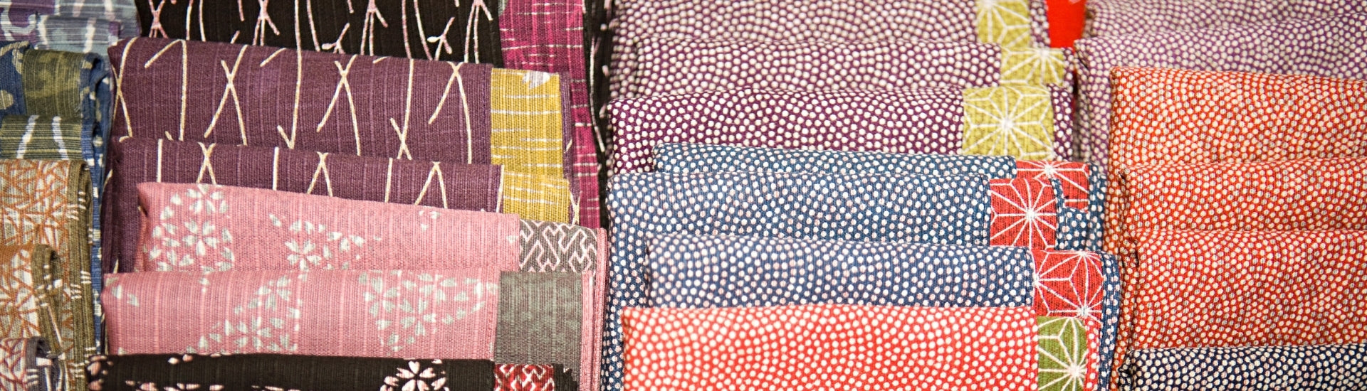 Close-up of assorted Japanese textiles and patterned fabrics arranged in rows, featuring traditional designs and colors