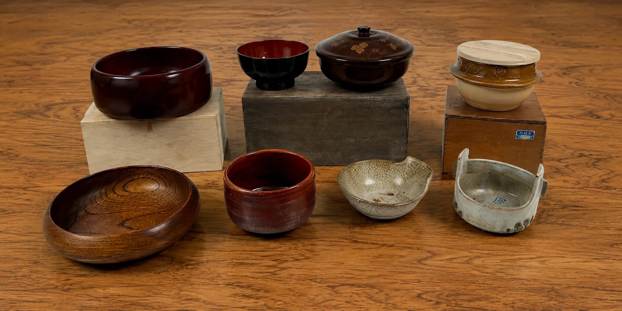 Vintage Japanese bowls in lacquerware, ceramic, and wooden designs displayed on a warm wooden tabletop.