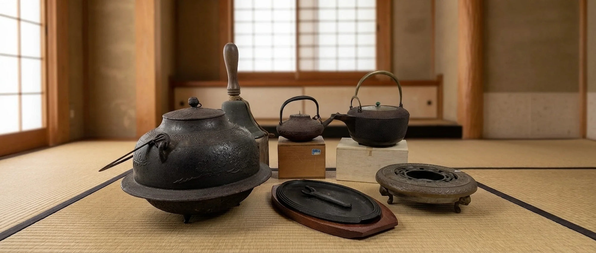 Collection of vintage Japanese metal items including cast iron kettles, tetsubin, bronze bell, brazier, and traditional metalware displayed in a traditional Japanese room setting