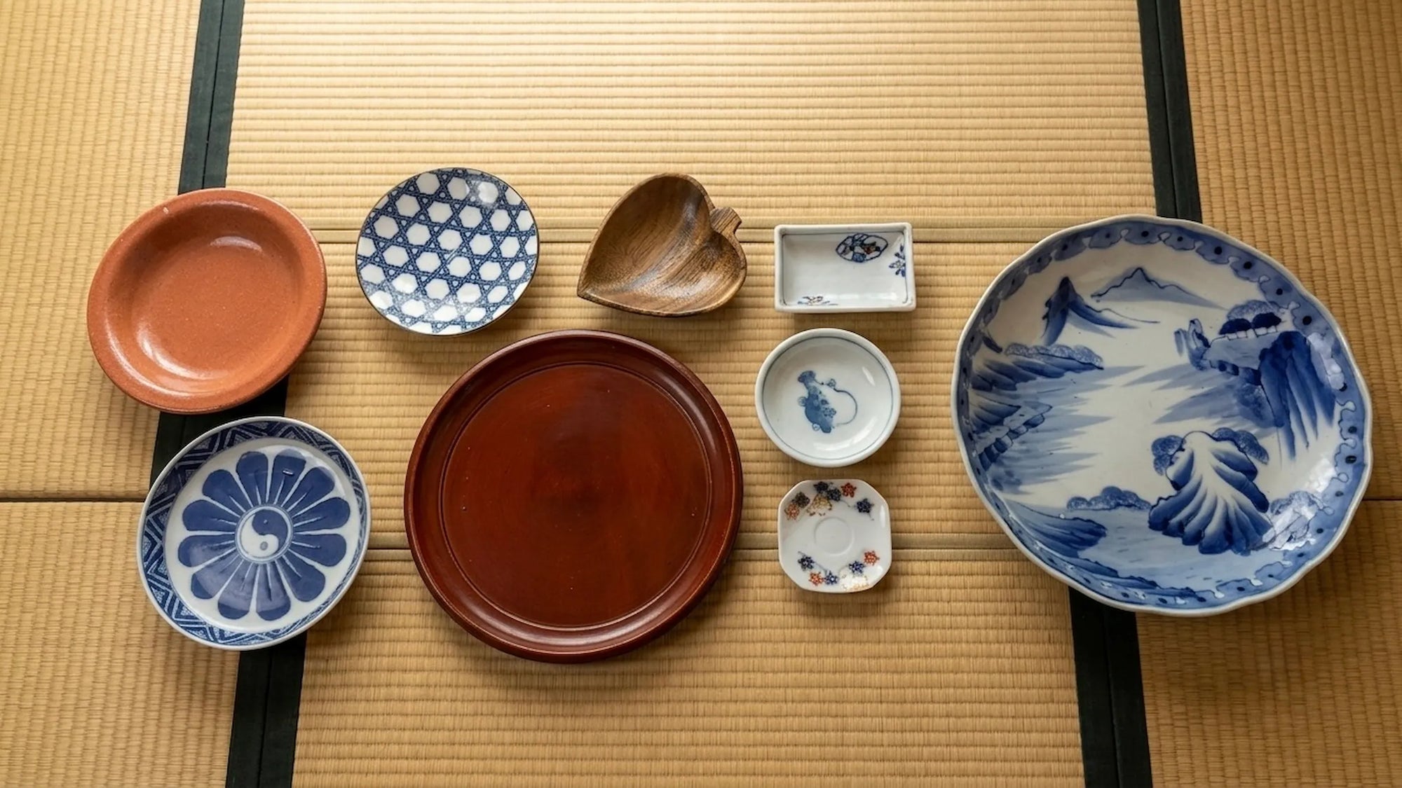 Collection of vintage Japanese plates, serving dishes, lacquer trays, and decorative tableware displayed in a traditional Japanese setting