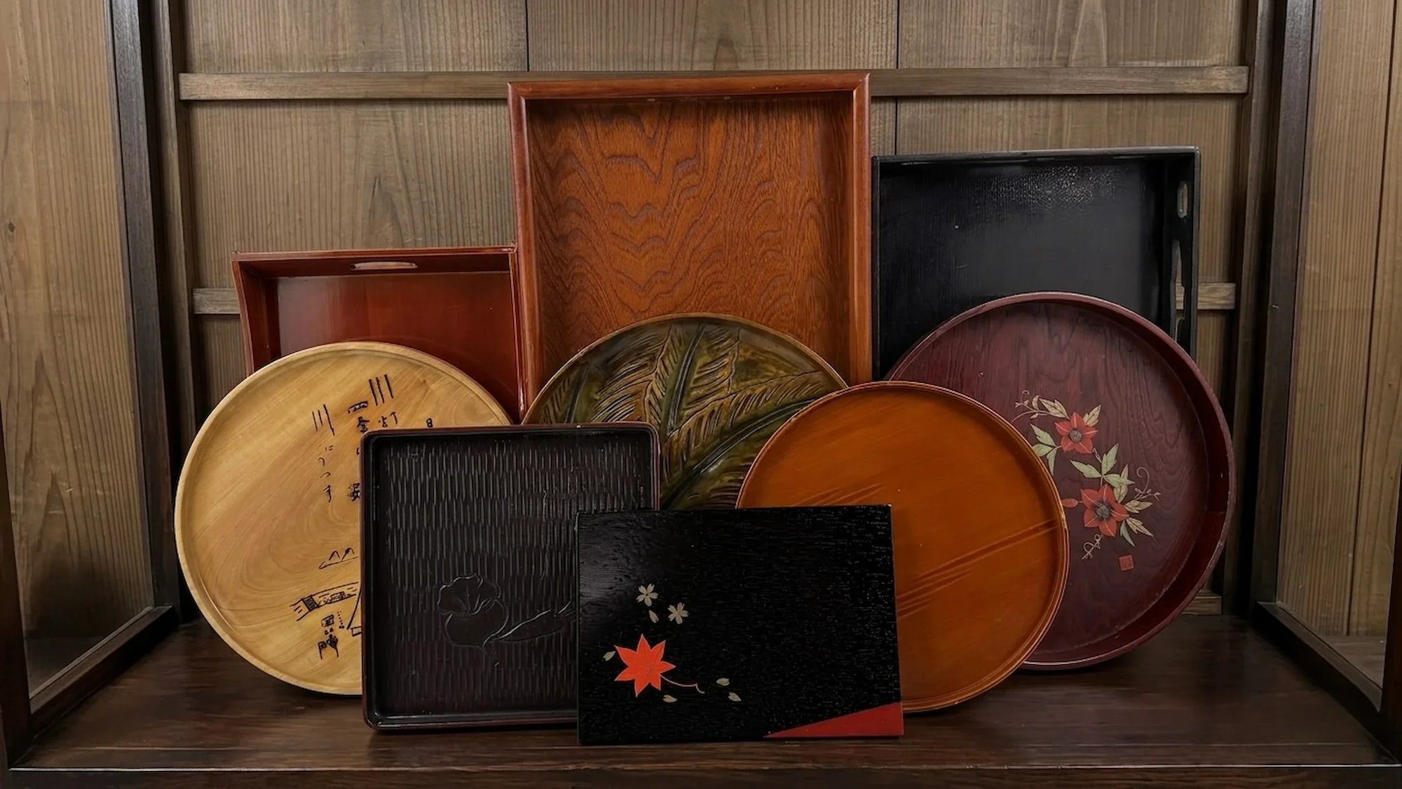 Collection of vintage Japanese serving trays and lacquerware trays displayed in a traditional wooden cabinet.
