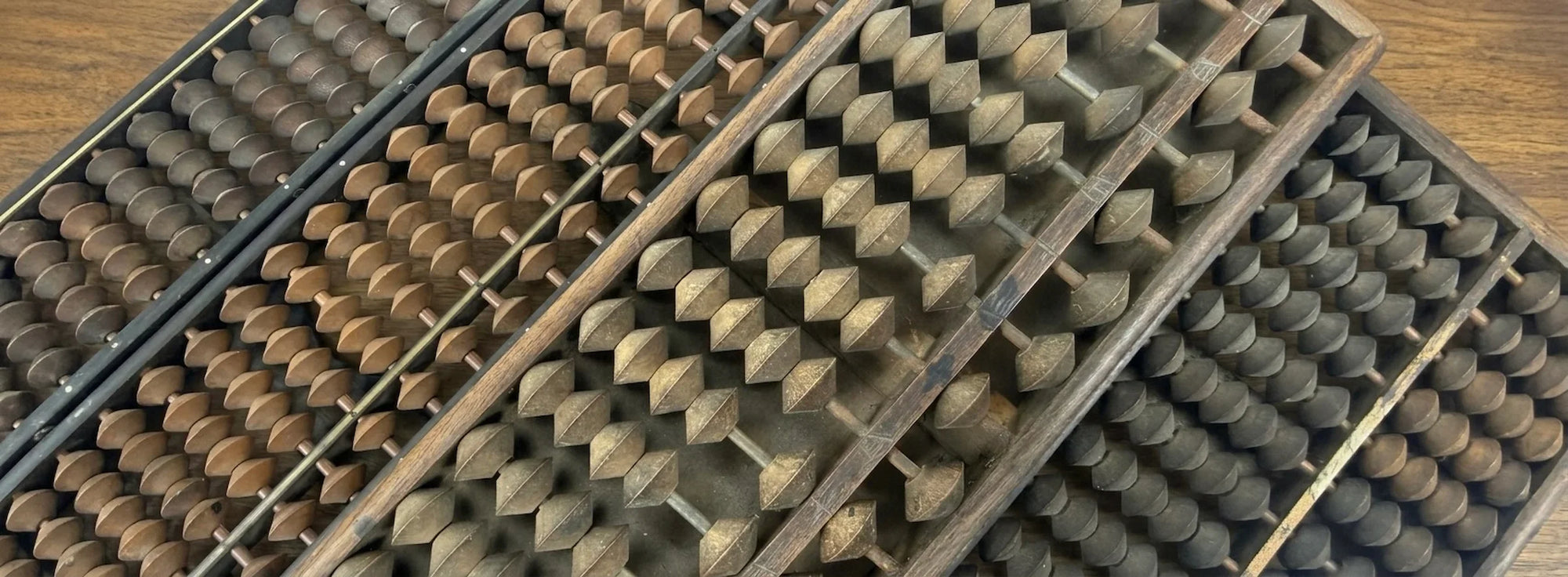 Vintage Japanese soroban abacuses arranged diagonally on a wooden tabletop, highlighting traditional calculation tools and craftsmanship.