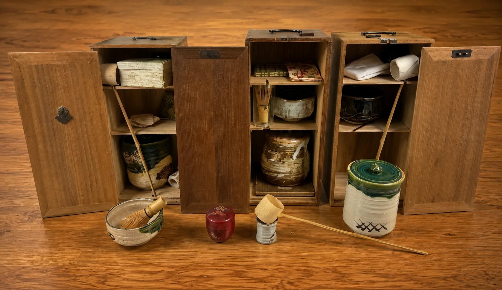 Vintage Japanese tea ceremony sets and tea utensils displayed in traditional wooden storage boxes on a warm wooden tabletop.
