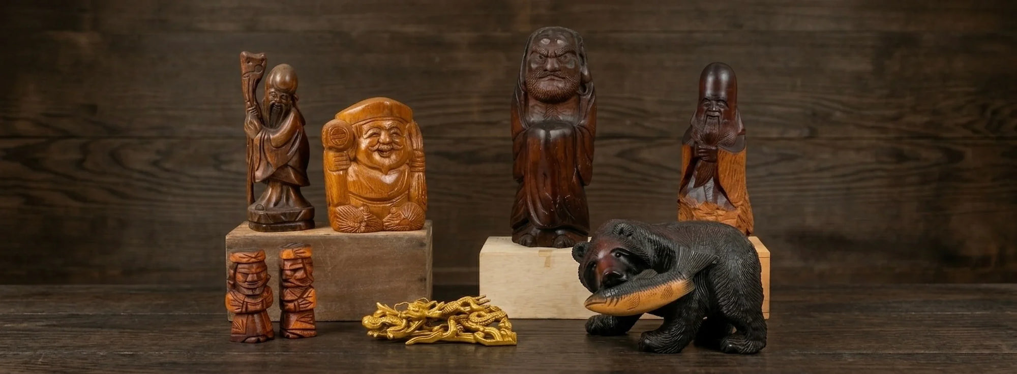 Collection of vintage Japanese wood carvings including folk art figures, a carved bear, and decorative sculptures displayed against a dark wooden background.